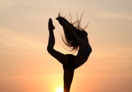 woman midair in an acrobatic pose on a beach at sunset